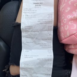Anything with a "0.00" is an item we ordered but was removed without the groups knowledge. - A crumpled receipt from Taino's Kitchen, located at 849 Mount Prospect Avenue, Newark, NJ, displays an order including Caribbean dishes such as pollo, arroz blanco, and tamarindo, with prices and quantities. The receipt includes transaction details, subtotal, sales tax, and total amount paid via debit card. The background shows part of a person's lap, with a pink patterned bag and black clothing visible.