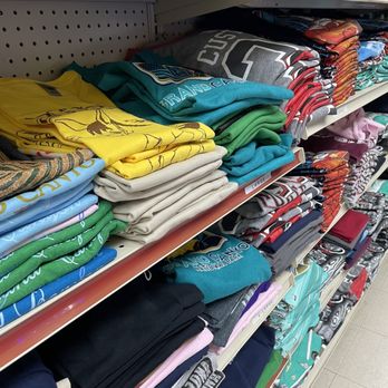 Texaco Express Mart - Multiple shelves display folded T-shirts and clothing items in various colors and designs at a retail store. - Gas Stations Near Me - Tusayan, Arizona