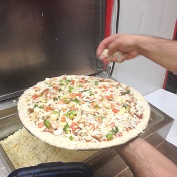 Dillo's Pizza - a person putting toppings on a pizza - Pizza Near Me - Calgary, Alberta