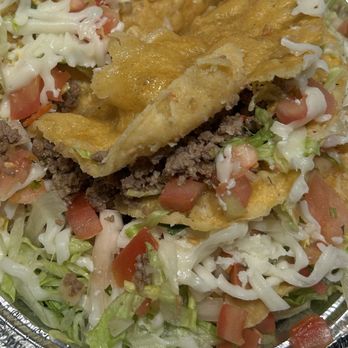 Metate - Hard shell ground beef tacos - I think - A taco filled with seasoned ground beef, topped with shredded lettuce, diced tomatoes, and shredded cheese, served in a crispy taco shell inside a foil container. The image shows fresh ingredients and typical taco toppings. - Mexican Near Me - Bronx, New York