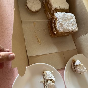 Miski Bakery - Alfajores, Milhojas/Napoleons Lucuma & dulce de leche. - Assorted desserts topped with powdered sugar, placed on plates and in a cardboard box, with some crumbs visible. - Bakeries Near Me - Chicago, Illinois