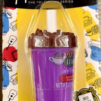 Dollar Tree - Iced coffee lip balm - The image shows a lip balm product in a purple container designed to resemble a coffee cup, with a chocolate-colored lid mimicking whipped cream. The packaging features branding from the Friends TV series, including the show's logo and related graphics. The product is labeled as iced coffee flavored and has a net weight of 0.14 ounces (4 grams). The packaging includes colorful illustrations and branding elements associated with the series. - Discount Store Near Me - Derwood, Maryland