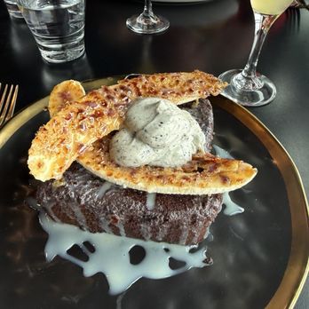 VUE Rooftop - French toast - Chocolate cake topped with ice cream, caramelized bananas, and a white sauce, served on a black plate with a gold rim. - New American Near Me - Washington, DC, District of Columbia
