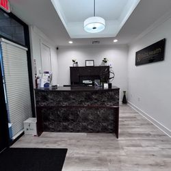QuCiL Health™ - The image shows the inviting reception area of QuCiL Health™. A dark, marble-patterned front desk sits opposite the entrance....
