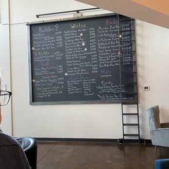 Trellis Wine Bar - a chalkboard with a list of wines on it - A blackboard menu displays wine options, cheeses, and upcoming events at a wine bar, with a ladder leaning against the wall. - Wine Bars Near Me - Denver, Colorado