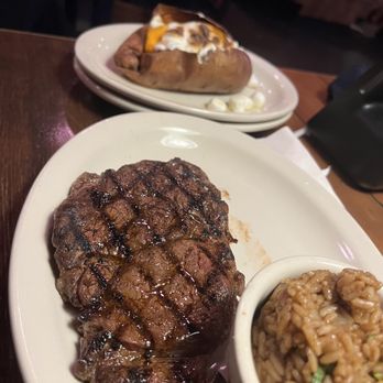 Texas Roadhouse - Ribeye - A meal featuring a grilled steak, a bowl of seasoned rice, and a baked potato topped with cheese, sour cream, and other toppings. - Steakhouses Near Me - Clovis, New Mexico