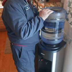Distillata - Distillata Water delivery driver loading a 5-gallon water bottle on a stainless steel water cooler