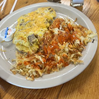 Pena's Place - Breakfast - A breakfast plate includes scrambled eggs with mushrooms, served alongside hash browns topped with ketchup. The plate is on a wooden table, with salt and pepper shakers, a sugar dispenser, and condiment packets visible in the background. The setting appears to be a casual dining environment. - New Mexican Cuisine Near Me - Ruidoso, New Mexico