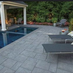 The Freedom Group Builders - This image showcases a luxurious outdoor living space featuring a blue swimming pool with expansive gray paver decking...