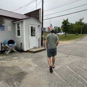 Annie's Overflow - Front entrance - A man in casual clothing walks towards a small, white building with an 'Open' sign, situated near a parking lot and utility poles. - Breakfast & Brunch Near Me - Holderness, New Hampshire