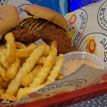 Dave's Hot Chicken - A basket containing crinkle-cut French fries, fried chicken tenders, and a small sandwich with pickles, served with a side of dipping sauce. - Chicken Shop Near Me - Dedham, Massachusetts