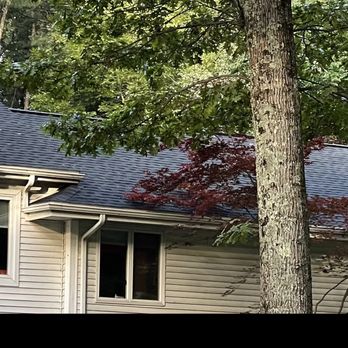 Golden Group Roofing - A house with white siding, a dark gray roof, and multiple windows, situated among tall trees in a wooded area. - Roofing Near Me - Hudson, Massachusetts