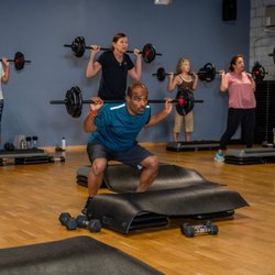 Cornerstone Health & Fitness - Members perform barbell squats during a group fitness class at our gym in New Hope, featuring polished wood floors, blue-gray...