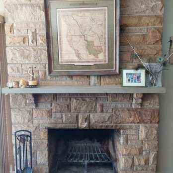 Sackett's Fireplace - A stone fireplace features a framed map above and a photo and decorative items on the mantel, with a fireplace grate inside. - Fireplace Services Near Me - Kalamazoo, Michigan