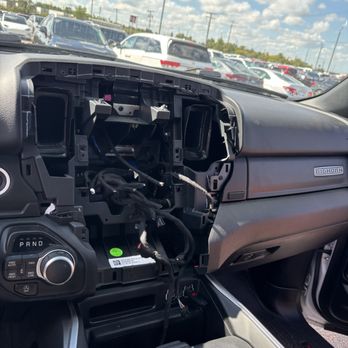 US Park - The vehicle's dashboard is disassembled, revealing internal wiring and mounting points, with a parking lot visible through the windshield. - Parking Near Me - Romulus, Michigan