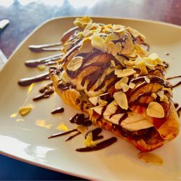Almandine - A dessert pastry with sliced almonds, drizzled with chocolate and caramel sauces, served on a white square plate.