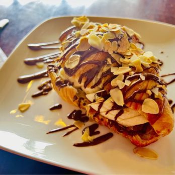 Beyond Cafe - Almandine - A dessert pastry with sliced almonds, drizzled with chocolate and caramel sauces, served on a white square plate. - Coffee & Tea Near Me - Orleans, Ontario