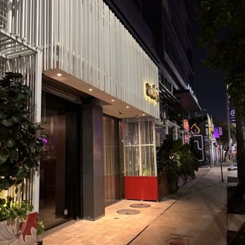 Uchi Miami - Exterior of a contemporary restaurant at night featuring vertical white slats, glass doors, and subtle lighting, with neighboring storefronts visible. - Japanese Near Me - Miami, Florida