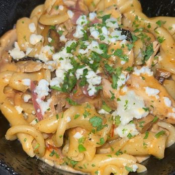 M'tucci's Italian - Chipotle Chicken Pasta (Campanelle Pollo alla Diavola) - A bowl of cooked pasta with a creamy sauce, garnished with crumbled cheese, chopped green herbs, and sliced vegetables. The dish is served in a black bowl, with visible sauce and toppings, indicating a flavorful pasta meal. - Italian Near Me - Albuquerque, New Mexico