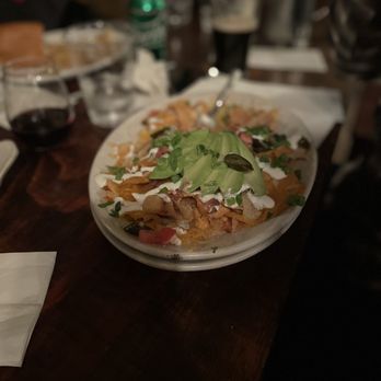 Murphys Irish Pub - Irish Nachos - A dish of Irish nachos with kettle chips, topped with lettuce, green onions, jalapeño slices, and drizzled with sauces, served on a white oval plate. - Irish Pub Near Me - Murphys, California