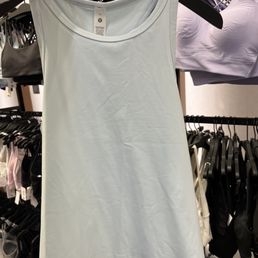 Lululemon Align Waist-Length Racerback - A plain white tank top is hanging on a black hanger in a retail store, with other clothing items and bras visible in the background.