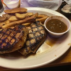 Salty Grilled pork chops with over cooked fries and pepper, pepper, onion, gravy on a sloppy plate.