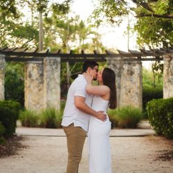 Ingraham Park - Female in white dress, male in white shirt & tan pants. They are kissing in the middle of the photo in front of columns.