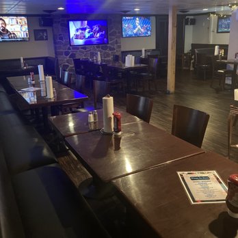 Wings On Main - Dining area - Dining area with dark wooden tables and chairs, paper towel rolls, condiments, and multiple TVs on the stone wall. - Chicken Wings Near Me - Hellertown, Pennsylvania