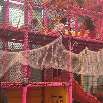 Antojitos - Play area - Children are engaging in activities on an indoor playground featuring pink and yellow structural elements, a slide, and a spider web climbing area. The playground is enclosed with black netting, and there are colorful support beams and a ceiling fan visible. The environment appears to be a family entertainment center or play area designed for children. - Mexican Near Me - Tucson, Arizona