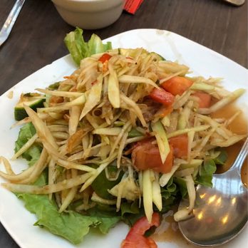 Paula's Thai Kitchen - papaya salad - A serving of papaya salad with shredded green papaya, tomatoes, and lettuce on a white plate, with a small bowl of sauce and utensils nearby. - Thai Near Me - Chicago, Illinois