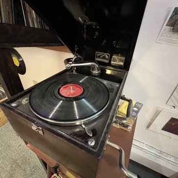 DVSTY Consignment - A vintage turntable with a black lid, a spinning vinyl record, and a tonearm, placed on a wooden surface. - Women's Clothing Near Me - Jamaica Plain, Massachusetts