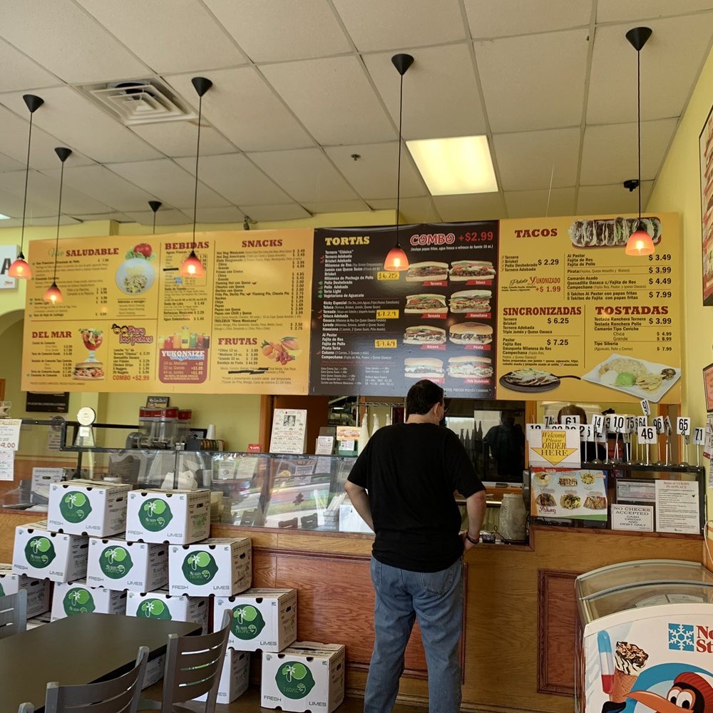 Tortas Yukon - a man standing in front of a menu - Mexican Near Me - Laredo, Texas Tortas Yukon - a man standing in front of a menu - Mexican Near Me - Laredo, Texas
