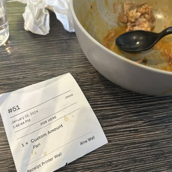 Los Taquitos - The image shows a white bowl with remnants of food and a black spoon inside, a crumpled napkin, and a receipt on a dark wooden table. - Mexican Near Me - Phoenix, Arizona