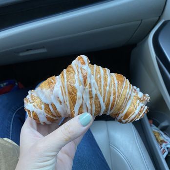 Bread - Almond croissant - A person holds a croissant with white icing drizzle inside a car, with the car's interior visible in the background. - Bakeries Near Me - Durango, Colorado