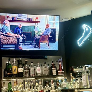 Gabagool Wine Bar - Bar - A bar area features a television displaying a scene from a TV show with three men and subtitles, along with a neon chili pepper sign on the wall. - Wine Bars Near Me - Fairfield, Connecticut