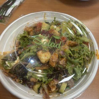 My Salad - Bbq Arcadian mix salad - A mixed salad with various greens, chopped vegetables, and toppings is contained in a clear plastic container with a lid labeled 'My Salad.' The container is placed on a wooden table, with another bowl of salad and some utensils visible in the background. - Salad Near Me - Wayne, New Jersey