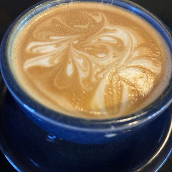 Blackbird Coffee House - Cappuccino - A close-up of a coffee beverage in a blue cup, featuring latte art with swirls and patterns, placed on a black saucer. - Coffee & Tea Near Me - Albuquerque, New Mexico