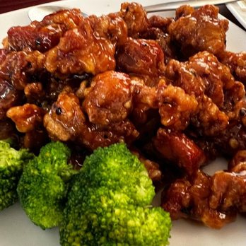 Dumpling House - General Gau's Chicken - A white plate holds a serving of General Gau's Chicken, featuring bite-sized pieces of fried chicken coated in a glossy, reddish-brown sauce. Fresh broccoli florets are placed on the side of the dish. The presentation suggests a Chinese restaurant setting, with the focus on the saucy chicken and vegetables. - Chinese Near Me - Newton, Massachusetts