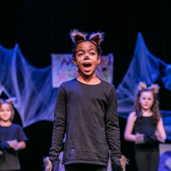 Imagination Stage - Girl with animal ears and facepaint, dressed in black, singing toward camera.  Other similar dressed kids in background