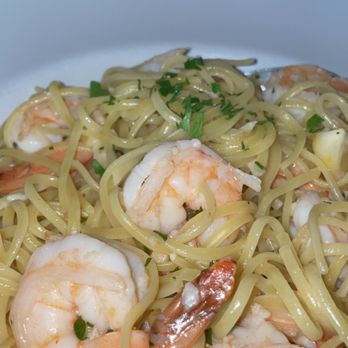 Victory Point - A seafood pasta dish featuring cooked shrimp and linguine, garnished with chopped herbs, served on a white plate. The background shows a dining setting with glasses and a view of Boston Harbor, indicating a waterfront dining venue offering New England-inspired cuisine. - Seafood Near Me - Quincy, Massachusetts