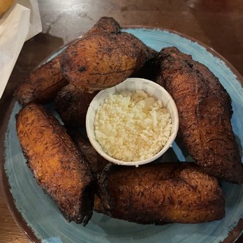 Guava Tree Cafe - Plantains - A plate of fried plantains with a side of grated cheese in a small cup, served on a blue ceramic plate. - Latin American Near Me - Albuquerque, New Mexico