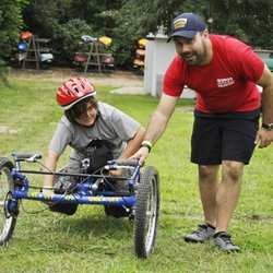 Adaptive Sports Connection - A volunteer help an athlete with trying out one of our adaptive mountain bikes.