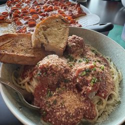Spaghetti and meatballs with pizza in the background