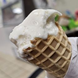 Katie'S Ice Cream &Chocolate --E - A Waffle Cone filled with a scoop of Coconut Ice cream in Close-up.