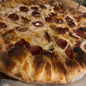 Logan’s Table - The gorg - A close-up of a pizza with a thick, golden-brown crust, topped with pepperoni slices, onions, and melted cheese. The pizza is placed on a metal tray on a wooden table, with a salad in a white bowl visible in the background. - New American Near Me - Leominster, Massachusetts