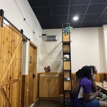 Squarrel Cafe - Wall - The image shows the interior of a cafe with wooden paneling, a ladder shelf, and two people sitting at a table. The ceiling is black with recessed lighting, and there is an air conditioning unit on the wall. - Coffee & Tea Near Me - Brooklyn, New York