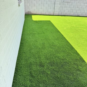 Alpha Turf - A backyard features bright green artificial grass bordered by a concrete block wall, with sunlight casting shadows. - Artificial Turf Near Me
