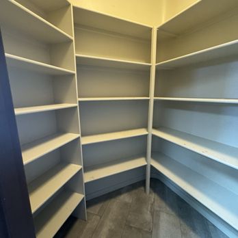 Trussell's Transformations - Before removing the shelves. - A small room features white corner shelves with multiple levels, and tiled flooring. The shelves are empty and the room appears to be a storage or pantry area. - General Contractors Near Me - Albuquerque, New Mexico