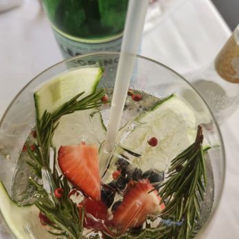 Atria - A glass of infused water contains cucumber slices, strawberries, blueberries, and sprigs of rosemary, with a straw inside. - New American Near Me - Edgartown, Massachusetts