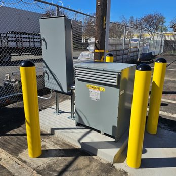Tarin Electric & Lighting - Outdoor electrical installation featuring a Square D transformer and control panel mounted on a concrete pad, secured with ye... - Electricians Near Me Tarin Electric & Lighting - Outdoor electrical installation featuring a Square D transformer and control panel mounted on a concrete pad, secured with ye... - Electricians Near Me